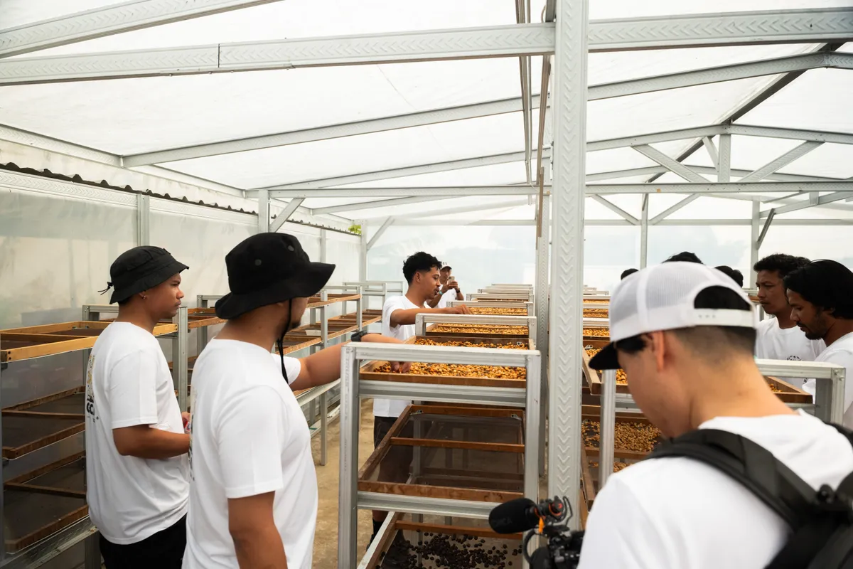 GCAG participants discussing coffee drying on raised trays inside a processing space.